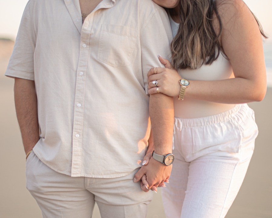 Engagement detail — interlaced hands and ring at the beach