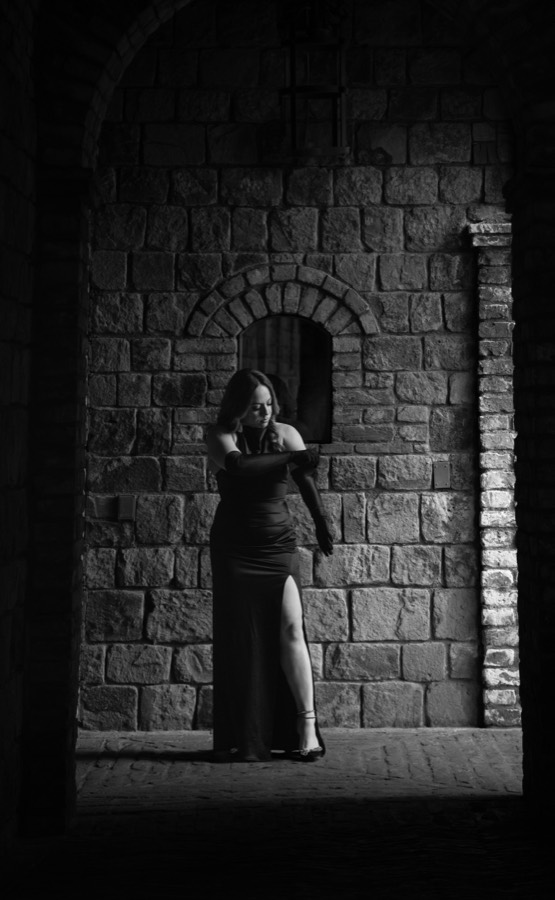 Black-and-white editorial portrait in a gown under a stone archway