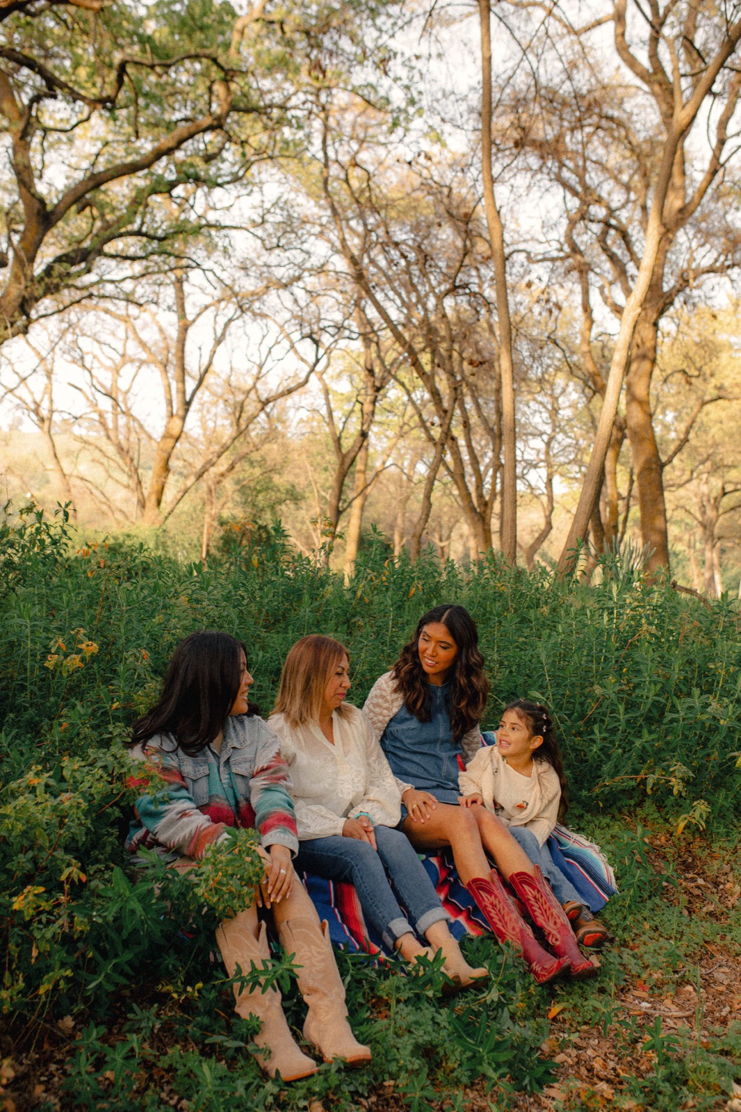 Family seated together on a blanket in a wooded grove at sunset