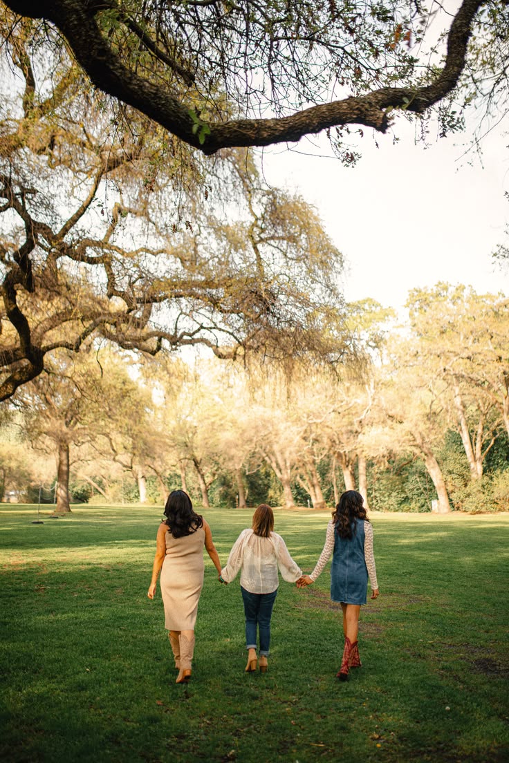 Three women holding hands walking through a sunlit park