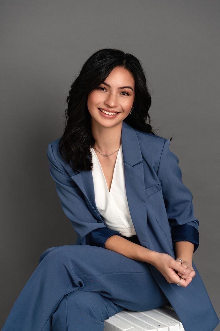 Studio headshot of a woman in a blue suit on a grey backdrop