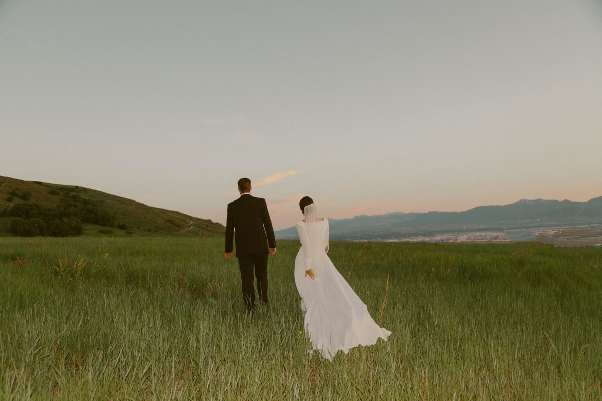 Bride and groom walking through a grassy hillside meadow at dusk
