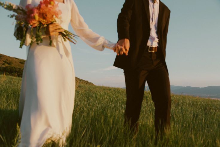 Bride and groom holding hands in a golden hillside field